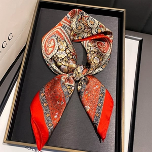 Macro detail of red and black paisley silk square scarf on a luxury black display tray