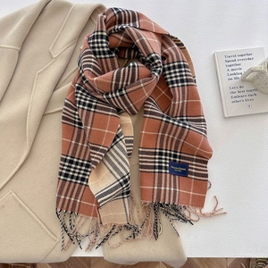 Detail van geruite sjaal met franjes en label op een zachte beige jas achtergrond