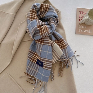 Detail van klassieke geruite sjaal met franjes en elegant label op een beige jas