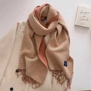 Detail of warm orange houndstooth scarf with tassels on elegant beige coat background