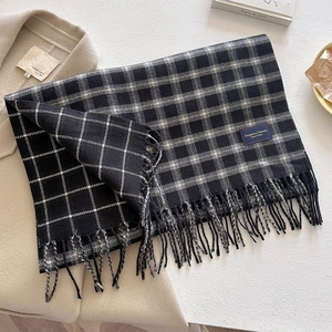Detail of dark blue and black plaid scarf featuring fine tassels and a soft fabric texture