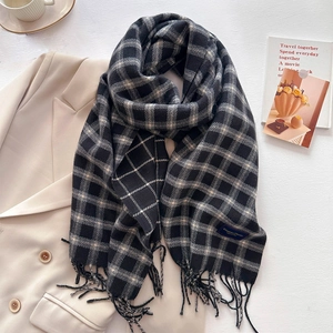 Close-up of black and white plaid scarf with tassels on beige blazer and lifestyle items