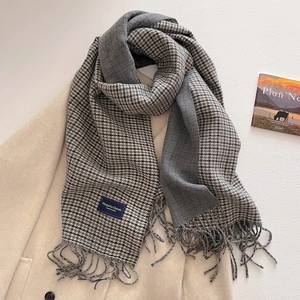 Detail of grey houndstooth scarf with fringe edge and label on ivory wool coat