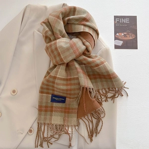 Close-up of thick plaid autumn scarf with fringes on beige blazer with elegant tag