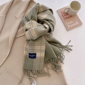 Detail of green plaid scarf with fringe and woven label on a cozy coat with coffee cup