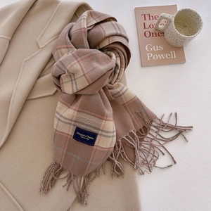 Detail of classic plaid scarf with fringe and elegant woven label on camel wool coat