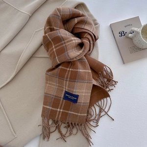 Detailed shot of caramel plaid scarf with fringe and a woven label on a wool coat