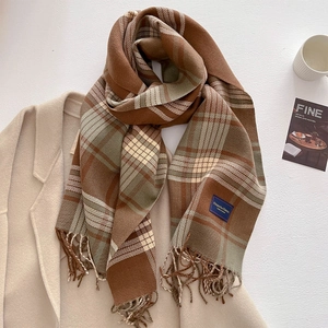 Close-up of earth-toned plaid scarf with fringe and 'Elegant & Classic' woven label