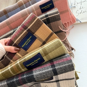 Stack of classic plaid cashmere-like scarves with fringe and brand label in warm colors