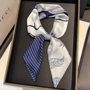 Detailed view of an elegant cream and navy silk scarf with leaf patterns on a display tray