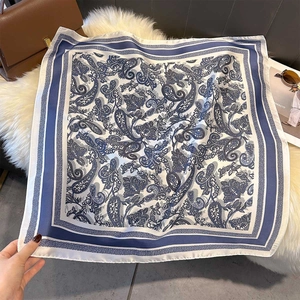 Detail of dark blue and white paisley silk scarf displayed on a soft plush background