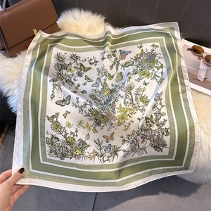 Detailed view of square faux silk scarf featuring green borders and floral butterfly patterns