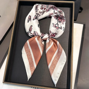 Detail of silk square scarf featuring floral prints and striped edges on a display tray