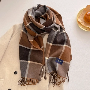 Detail of warm brown plaid scarf with fringe and blue label on white coat