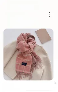 Detail of pink and grey plaid scarf featuring a classic woven label and soft tassel edges
