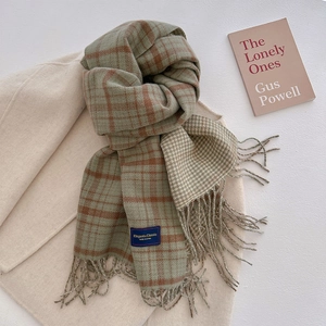 Classic green and orange plaid knit scarf with tassels laid on a beige coat