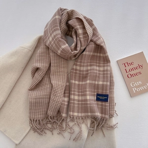 Detail of plaid tasseled scarf in earth tones layered on a stylish beige coat