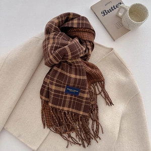 Close-up of brown plaid scarf with fringe detail and blue label on beige wool coat