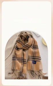 Detail of ginger plaid scarf with tassels and navy tag on a beige wool coat