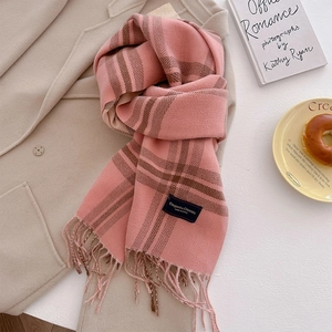 Close-up of pink and brown plaid cashmere-like scarf with fringe on a beige coat