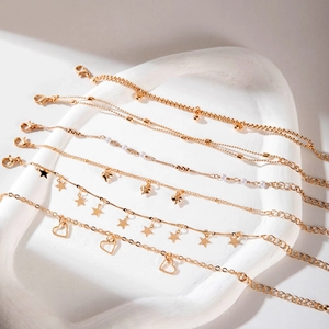 Detail of six gold-tone bracelets with heart and star charms on a white stone tray