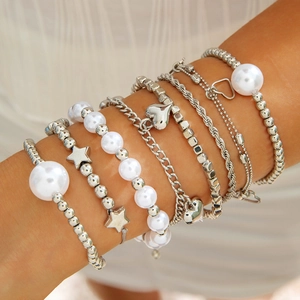 Close-up of layered silver bracelets with star heart charms and white pearls on wrist