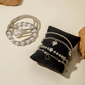 Close-up of stylish silver beaded bracelets with heart and star charms on a jewelry pillow