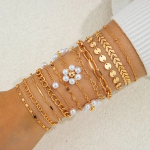 Close-up of layered gold beaded bracelets with pearls and heart fringe charms