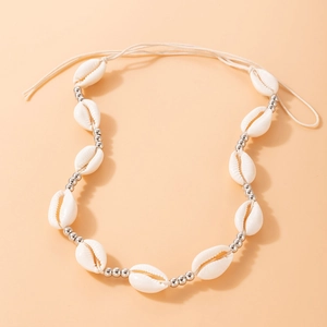 Detail of bohemian shell choker with white cowrie shells and silver beads on peach background