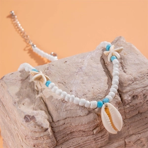 Detail of beach jewelry necklace featuring white beads, blue accents and a natural shell