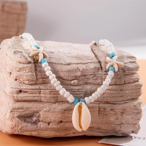 Detail of bohemian beach necklace with starfish charms and cowrie shell on rock