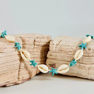 Detail of bohemian starfish beaded necklace with shells draped on natural ocean rocks