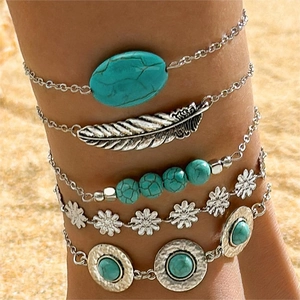 Bohemian silver anklet set featuring turquoise stones and feather charm on a beach