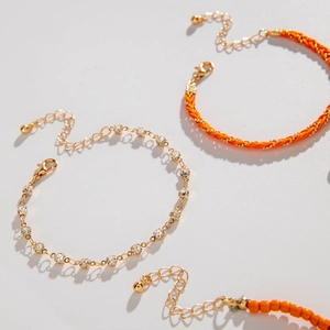 Detail of layered bohemian bracelets with beads, orange woven rope, and gold zircon chain