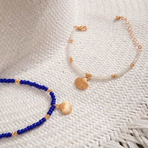 Detail of beach-style beaded bracelets with golden shell charms on a straw hat
