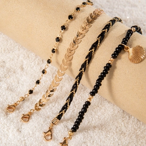 Detail of bohemian four-piece layered bracelets with black beads and gold shell pendant