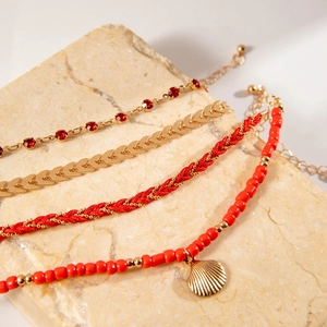 Detail of bohemian red beaded bracelet with gold shell charm and woven rope layers