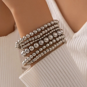 Close-up of stacked silver bead bracelets worn over a white ribbed sweater sleeve