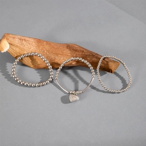 Macro shot of silver beaded bracelet set with heart pendant on natural bark background