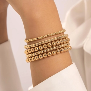 Five-piece set of gold beaded stackable bracelets with heart pendant worn by a model