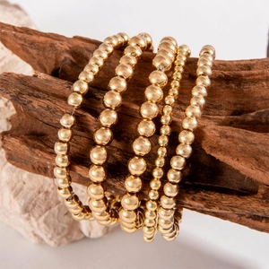 Detail of five-piece gold beaded elastic bracelets set draped on rustic wood texture