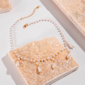 French style pearl necklace with gold metal links and teardrop pendants on a stone surface