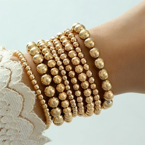 Macro shot of multilayered gold beaded bracelet stack with diverse bead sizes