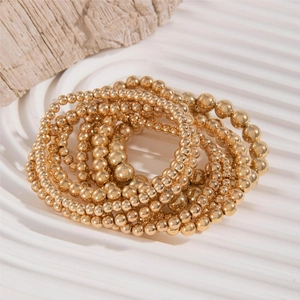 Detail of layered gold beaded bracelet stack featuring polished metallic mirror finish