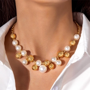 Detail of irregular pearl necklace with gold mirror beads on a white shirt background