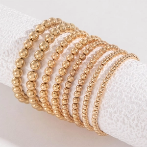 Detailed view of stacked gold beaded bracelets in various bead sizes on white stand