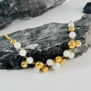 Detail of elegant gold beads and white pearls necklace draped over natural dark grey stone