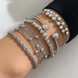 Detail of layered silver beaded bracelets with geometric charms on a woman's wrist