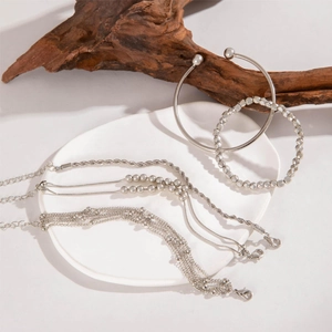 Close-up of silver beaded bracelets and heart pendant on white ceramic and wood