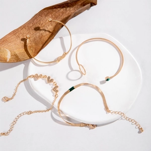 Four-piece gold bracelet set with green gemstones and heart pavé charms on white ceramic